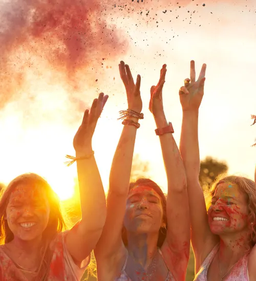 a sunset background with 3 girls in front, arms in the air in joy